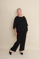 women wearing black pants and a black top and black heels on a neutral background