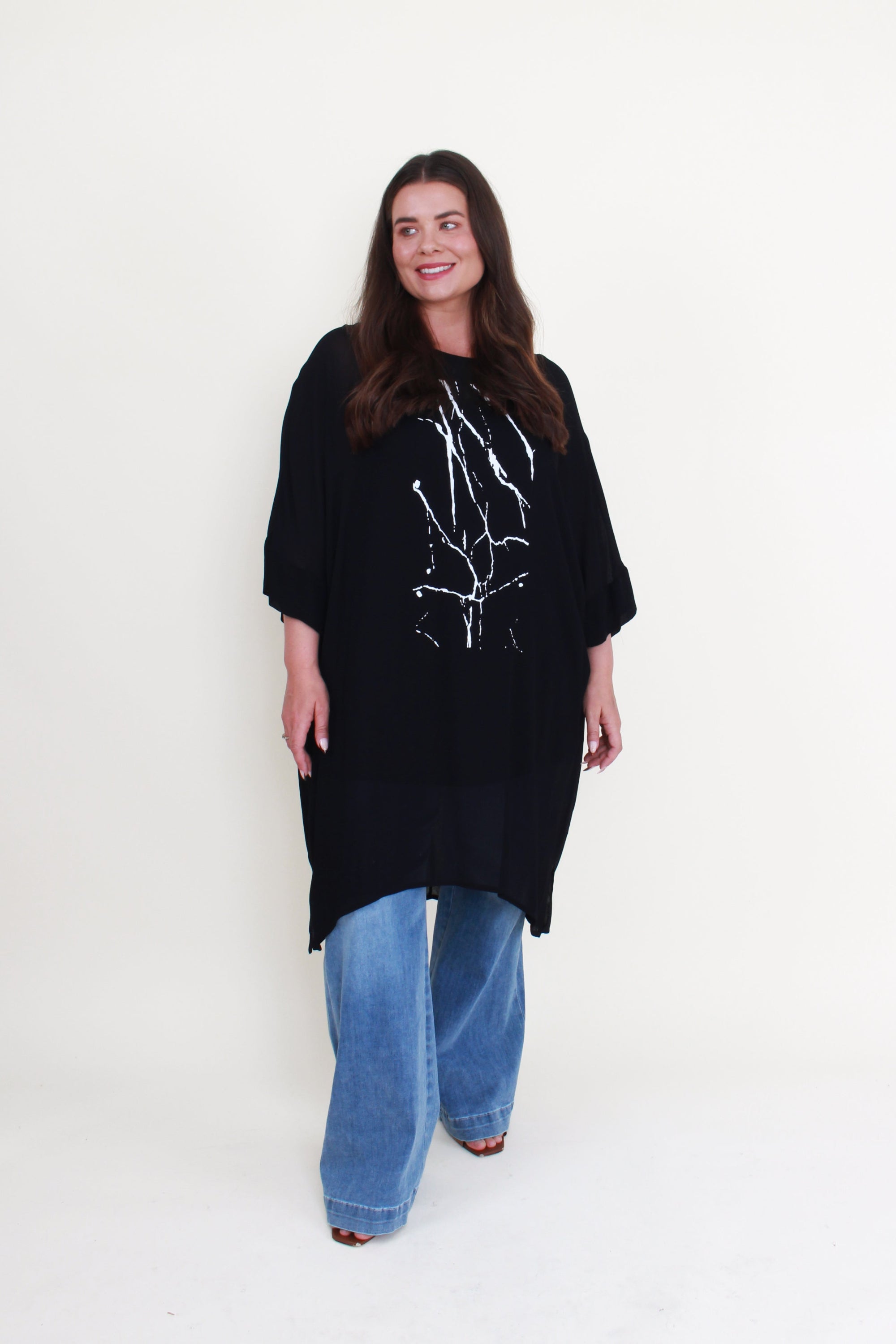 black tunic with white print and jeans worn by model 