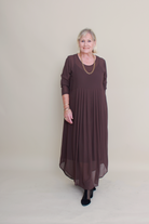 Woman wearing a long brown dress against a plain background