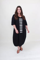lady in black cocoon dress with white graphic down the front on plain background