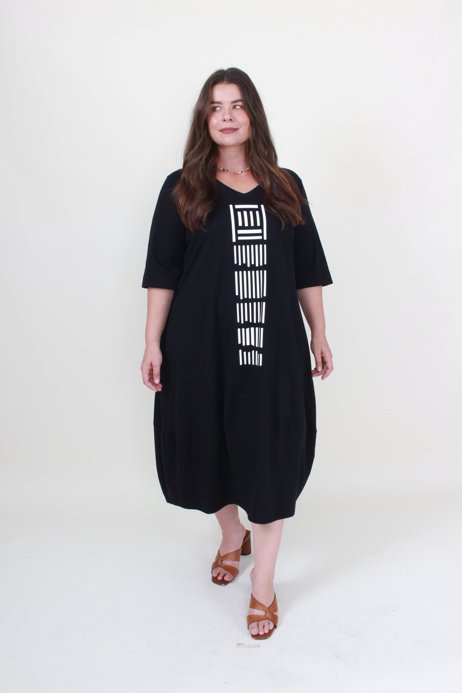 lady in black cocoon dress with white graphic down the front on plain background