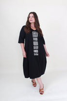 lady in black cocoon dress with white graphic down the front on plain background