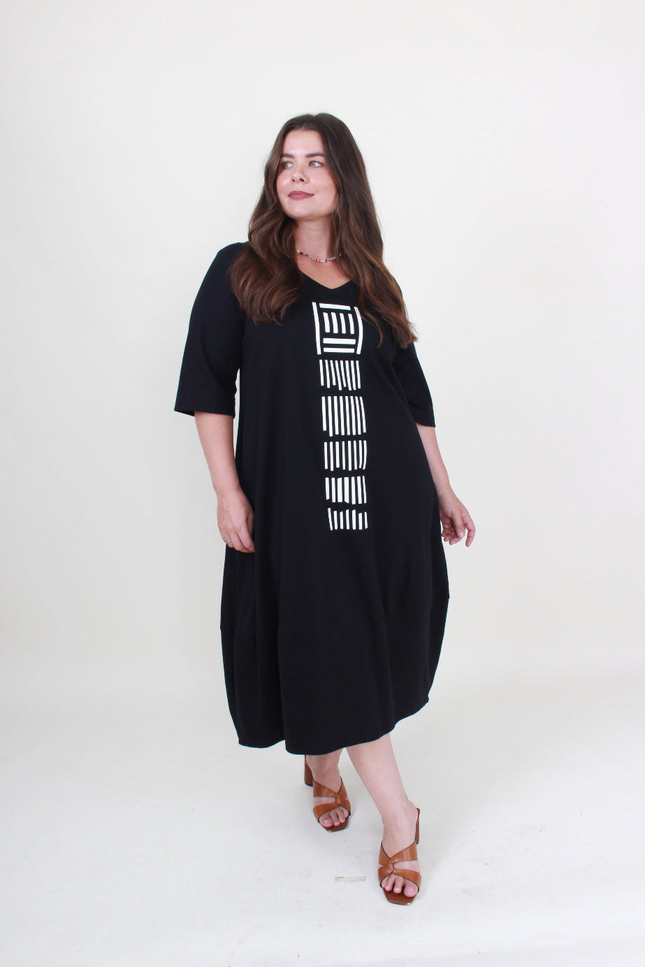 lady in black cocoon dress with white graphic down the front on plain background