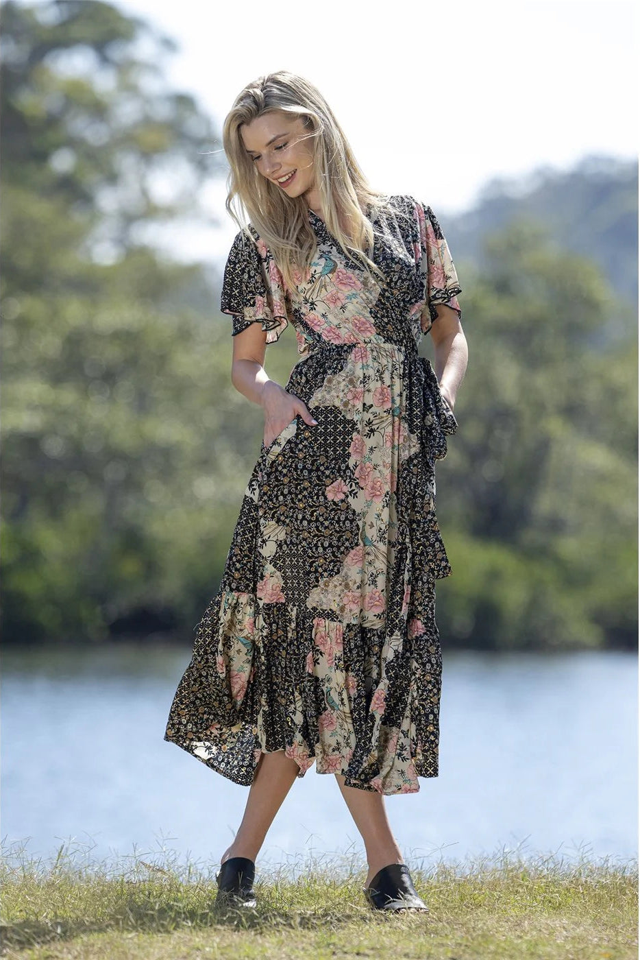 Woman in a floral dress standing by a lake with trees in the background