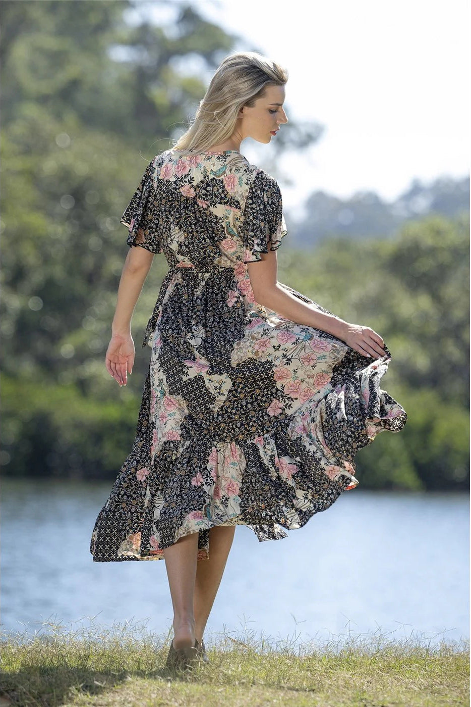 Woman in a floral dress standing by a lake with trees in the background