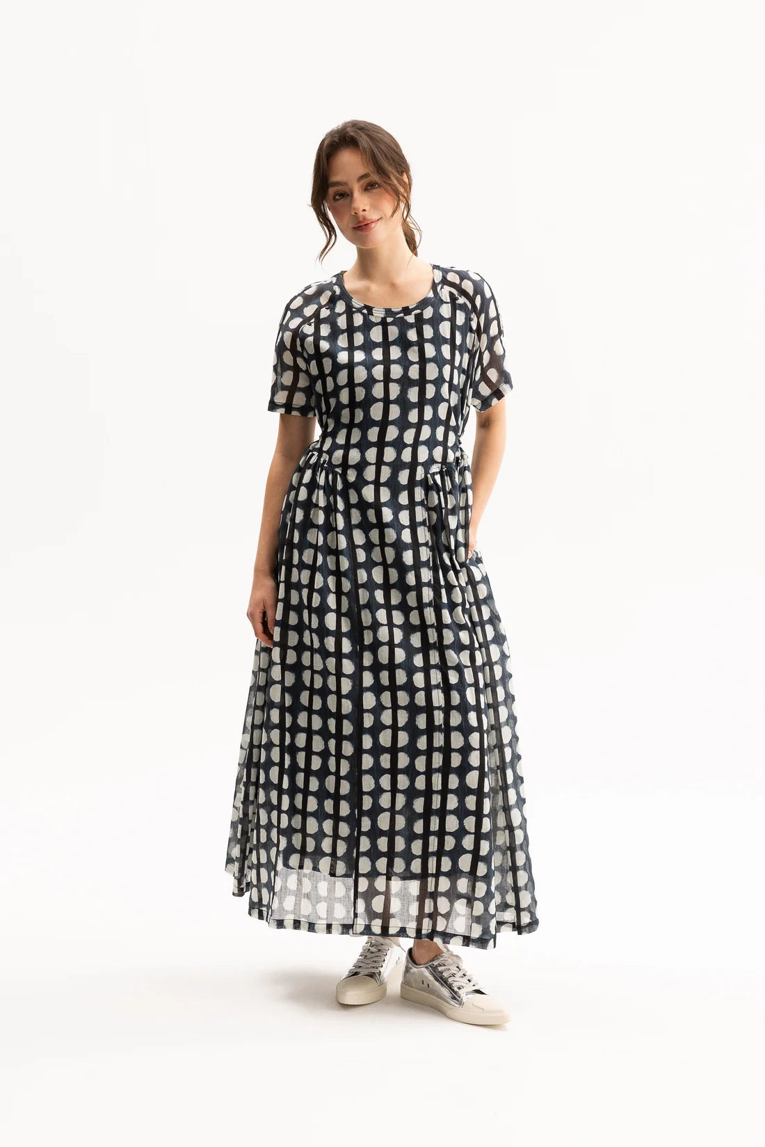 A woman modeling a short-sleeve midi dress with a black and white polka dot pattern, standing against a plain white studio background.