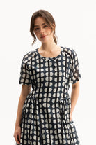 A woman wearing a short-sleeve dress with a black and white geometric pattern, standing against a plain white background.