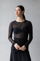 Woman wearing a black dress with sheer sleeves against a gray background