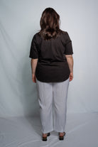 A woman viewed from behind wearing a black short-sleeve top and light gray wide-leg pants, standing against a light gray studio backdrop.