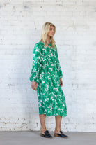 Woman wearing a green floral dress against a white brick wall.