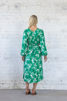 Woman wearing a green floral dress against a white brick wall back view