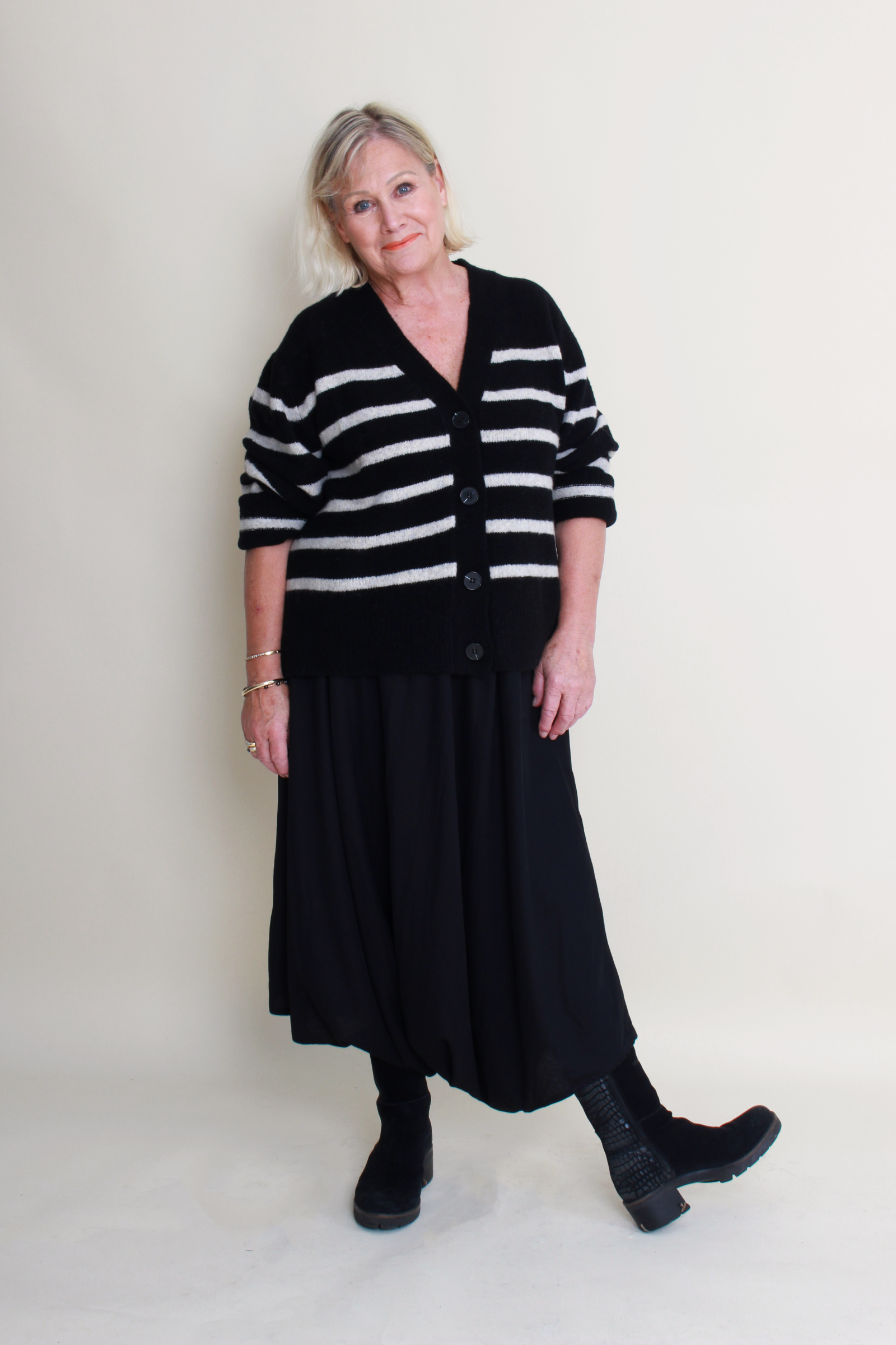 Woman wearing a black and white striped cardigan with a long black skirt on a plain background
