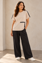 women wearing a beige tee shirt with black details and black pants on a beige background
