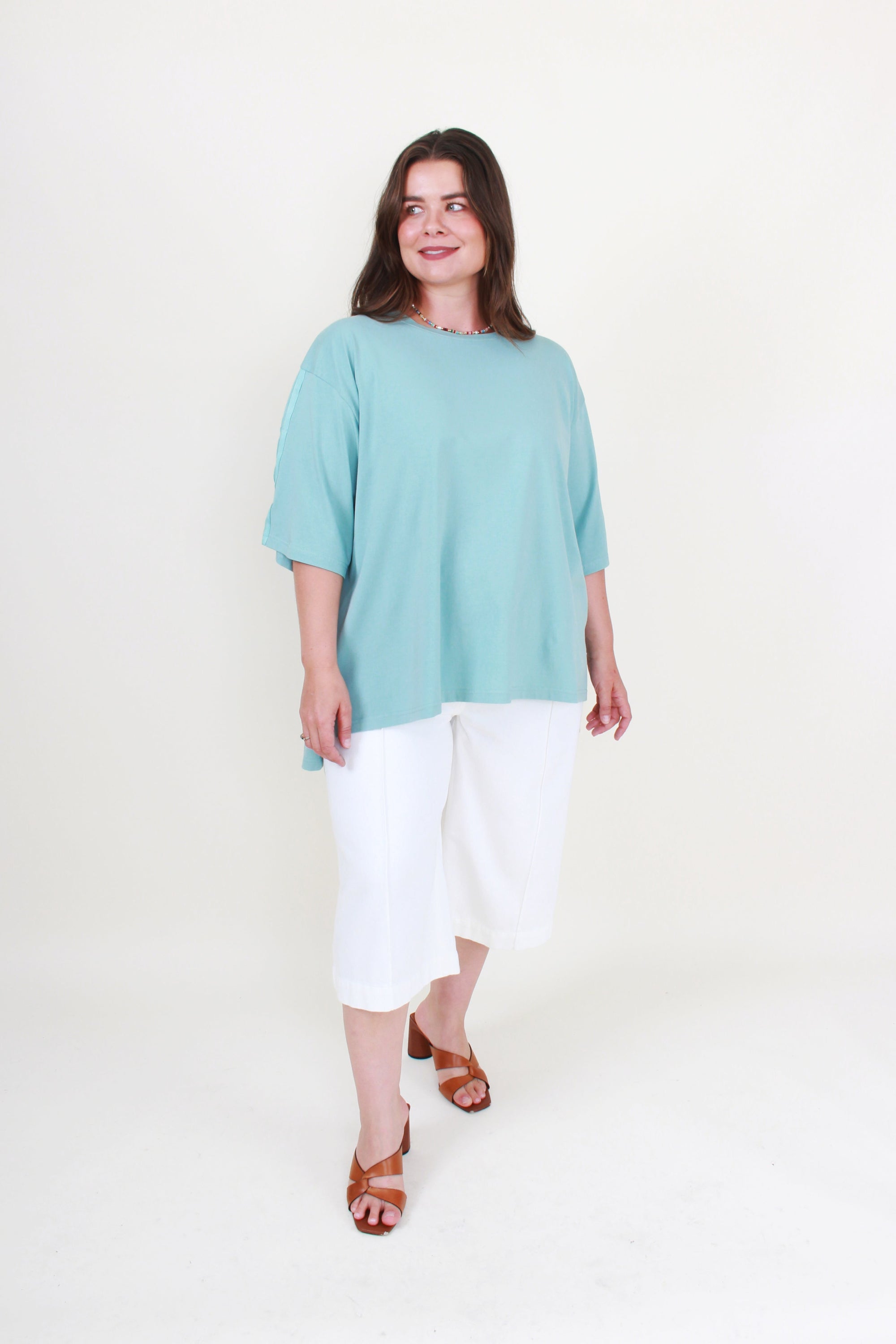 Woman wearing a light blue top and white pants on a white background
