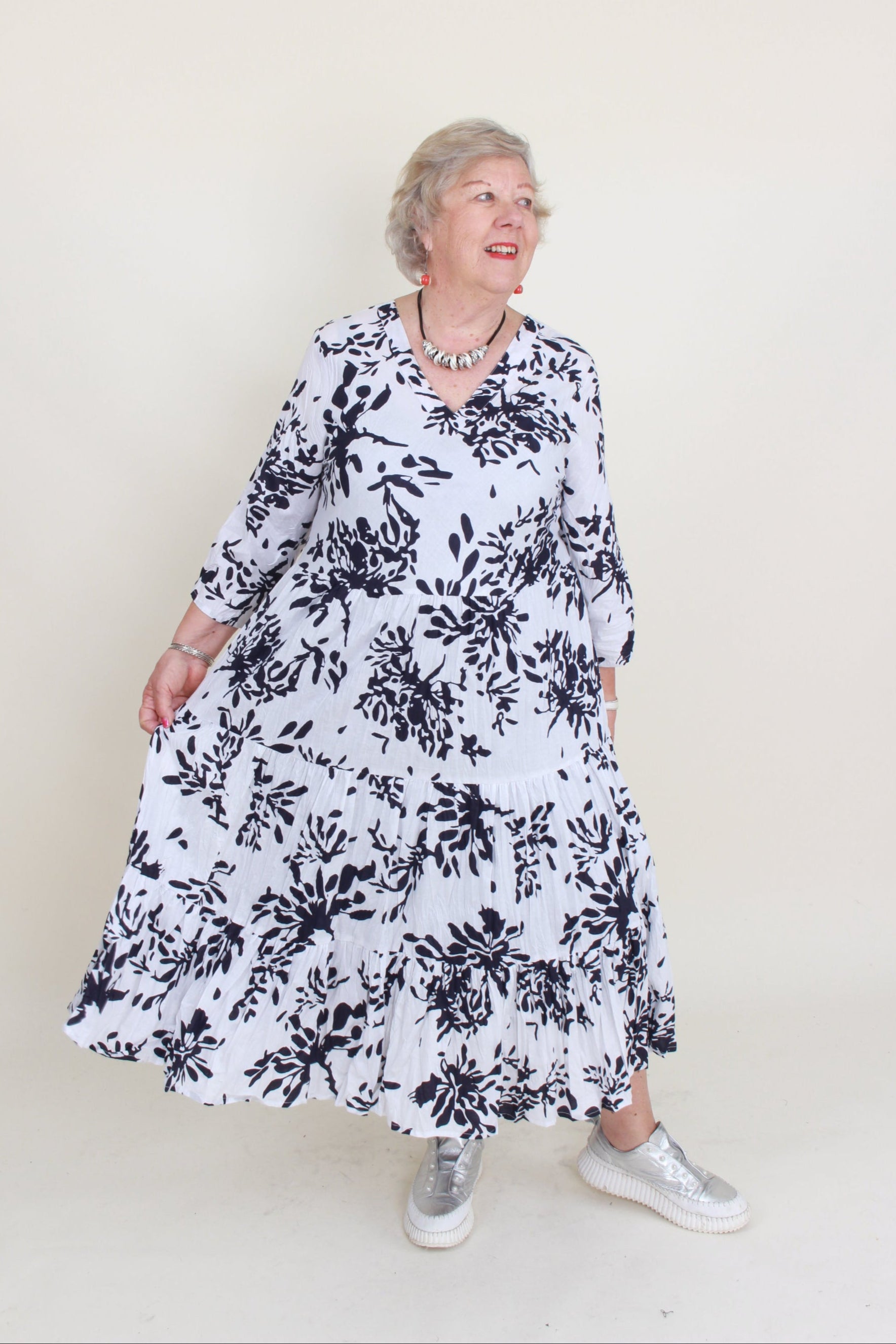 Person wearing a white dress with black floral pattern on a plain background
