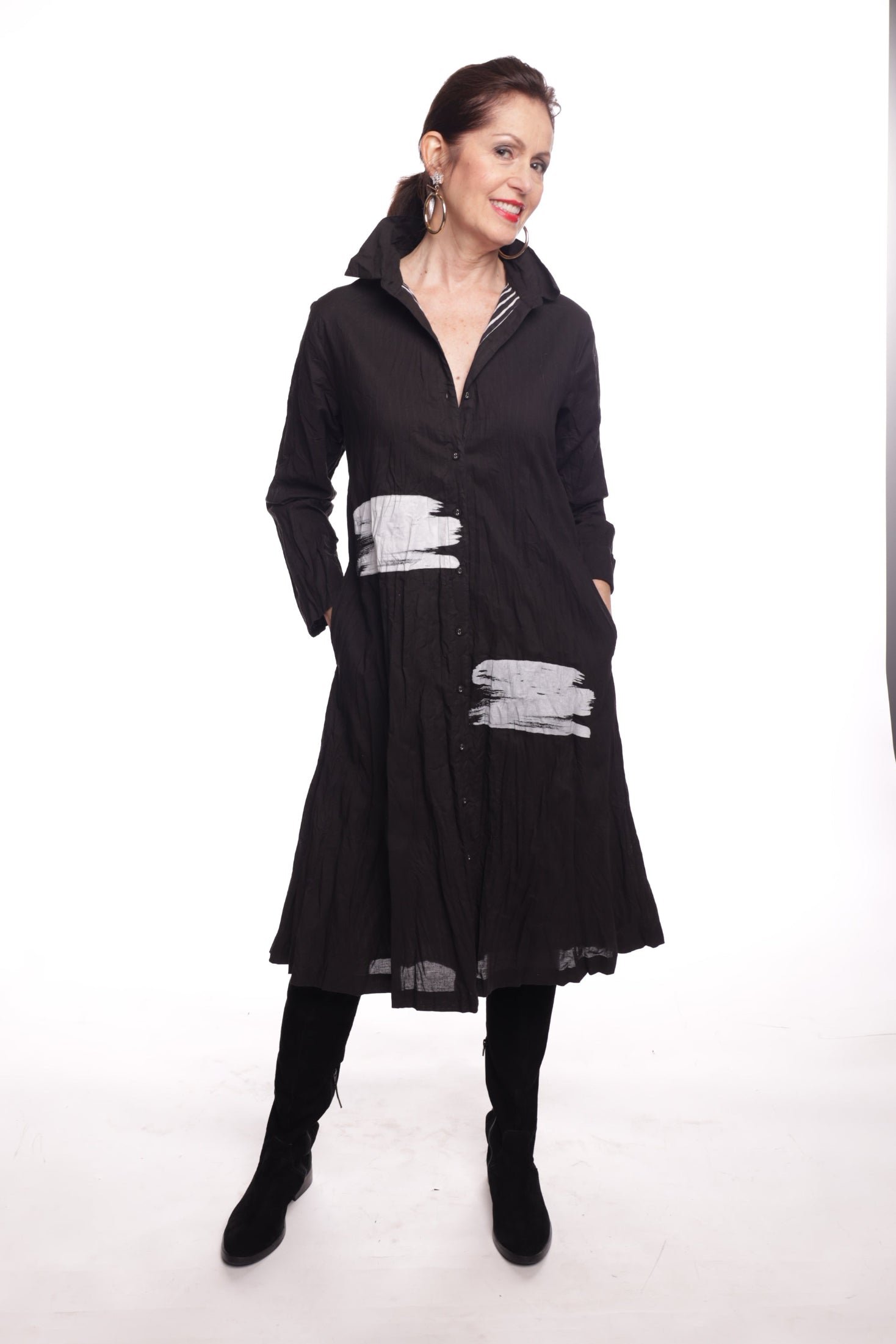 Women wearing a black shirt dress with white pattern and black boots on a plain white background