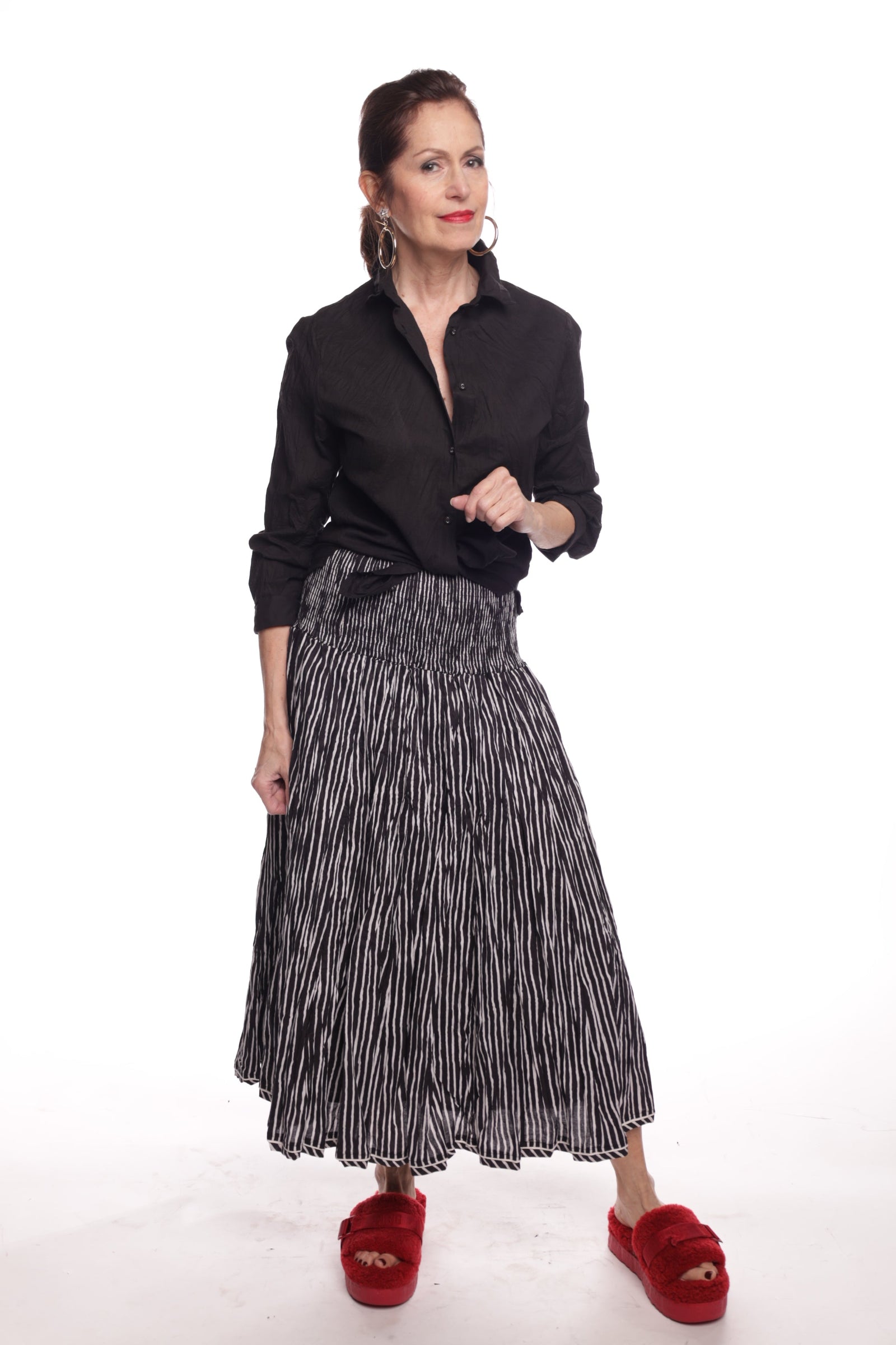 Person wearing a black shirt, black and white stripe skirt, and red shoes on a white background