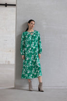 Woman wearing a green floral dress against a gray wall.
