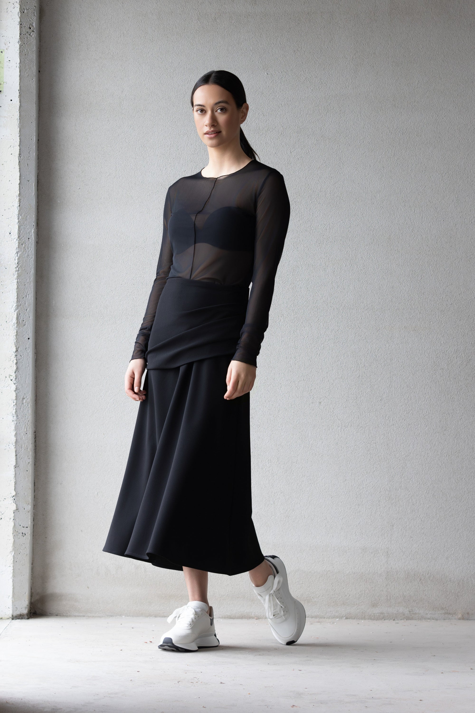 Woman wearing a black outfit with sheer panels against a plain background