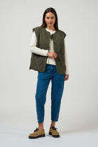 Woman wearing a green vest, white shirt, blue jeans, and brown shoes on a white background