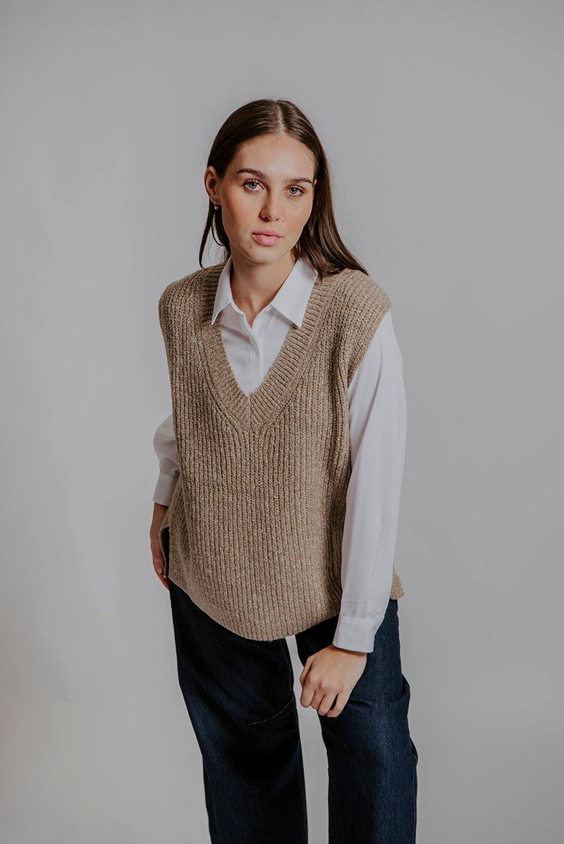 Woman wearing a beige knitted vest over a white shirt on a plain background