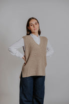 Woman wearing a beige knitted vest over a white shirt with a plain background