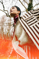 Person wearing a striped brown and off white shirt with a blurred background