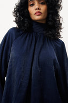 Person wearing a dark blue garment with a high neckline against a white background