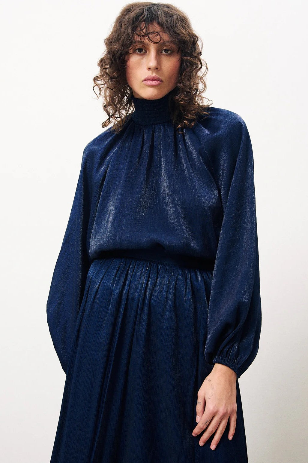 Woman wearing a dark blue dress with long sleeves against a white background