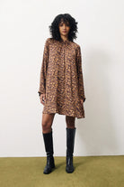 Woman wearing a leopard print dress and black knee-high boots against a white background