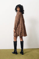 Woman wearing a leopard print dress and black knee-high boots on a white background