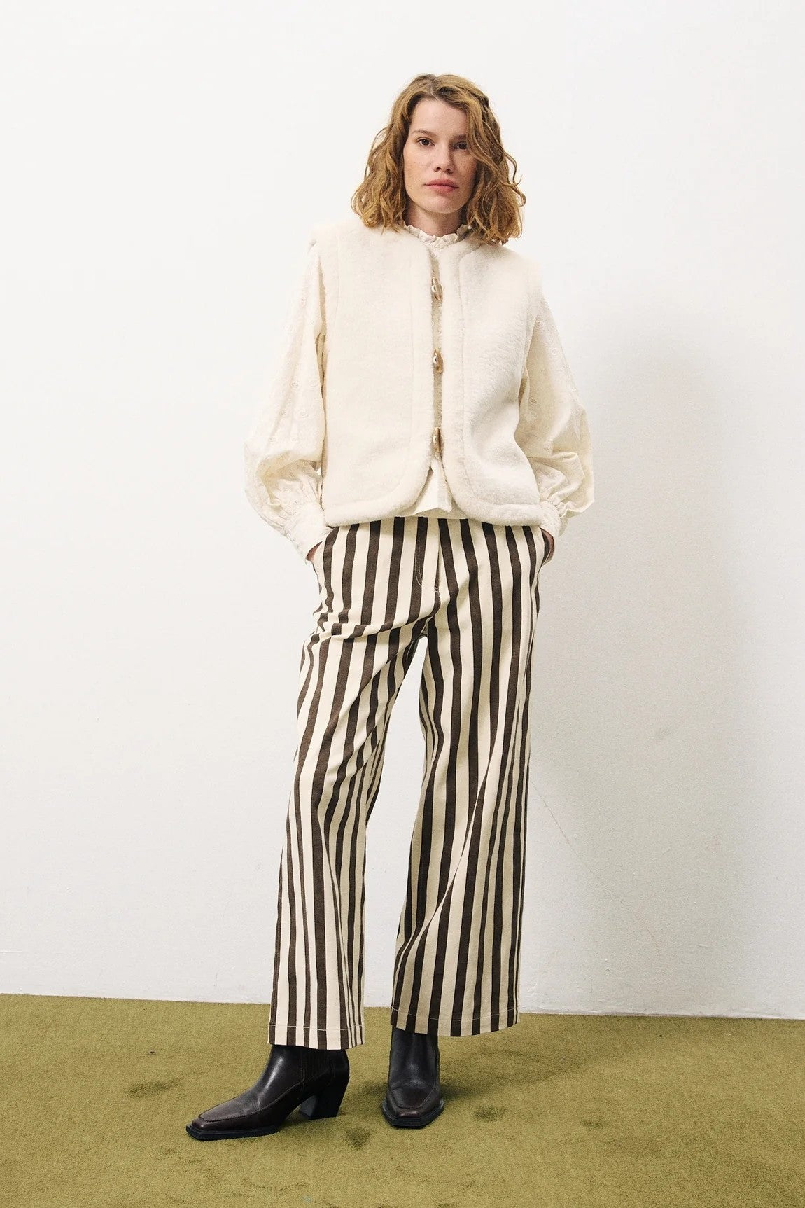 Person wearing a cream jacket and black and white striped pants against a white background