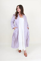 Woman wearing a long light purple coat over a white outfit on a white background