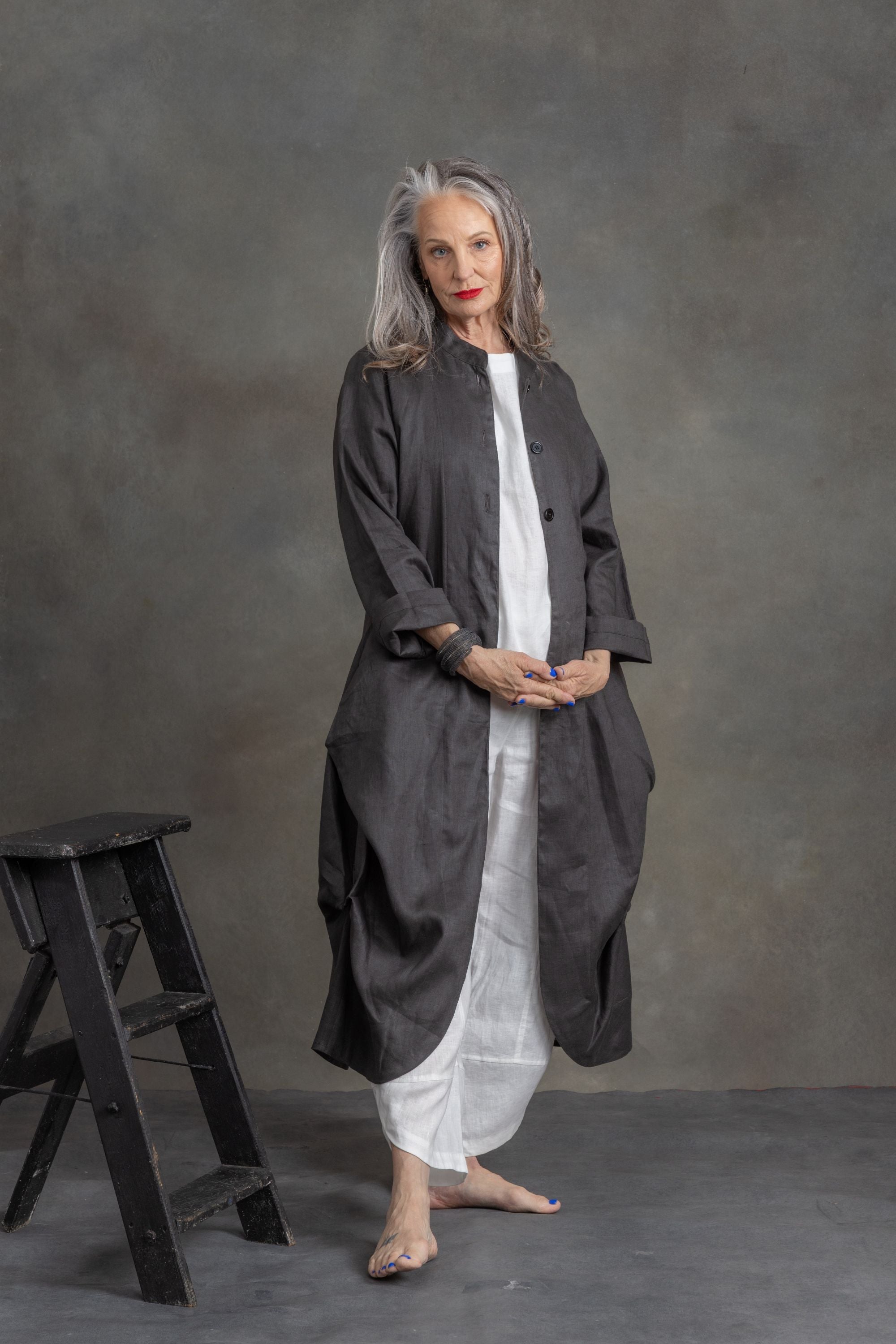 Woman wearing a long dark coat over a white dress against a gray background