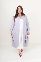 Woman wearing a long light gray coat over a white outfit on a white background