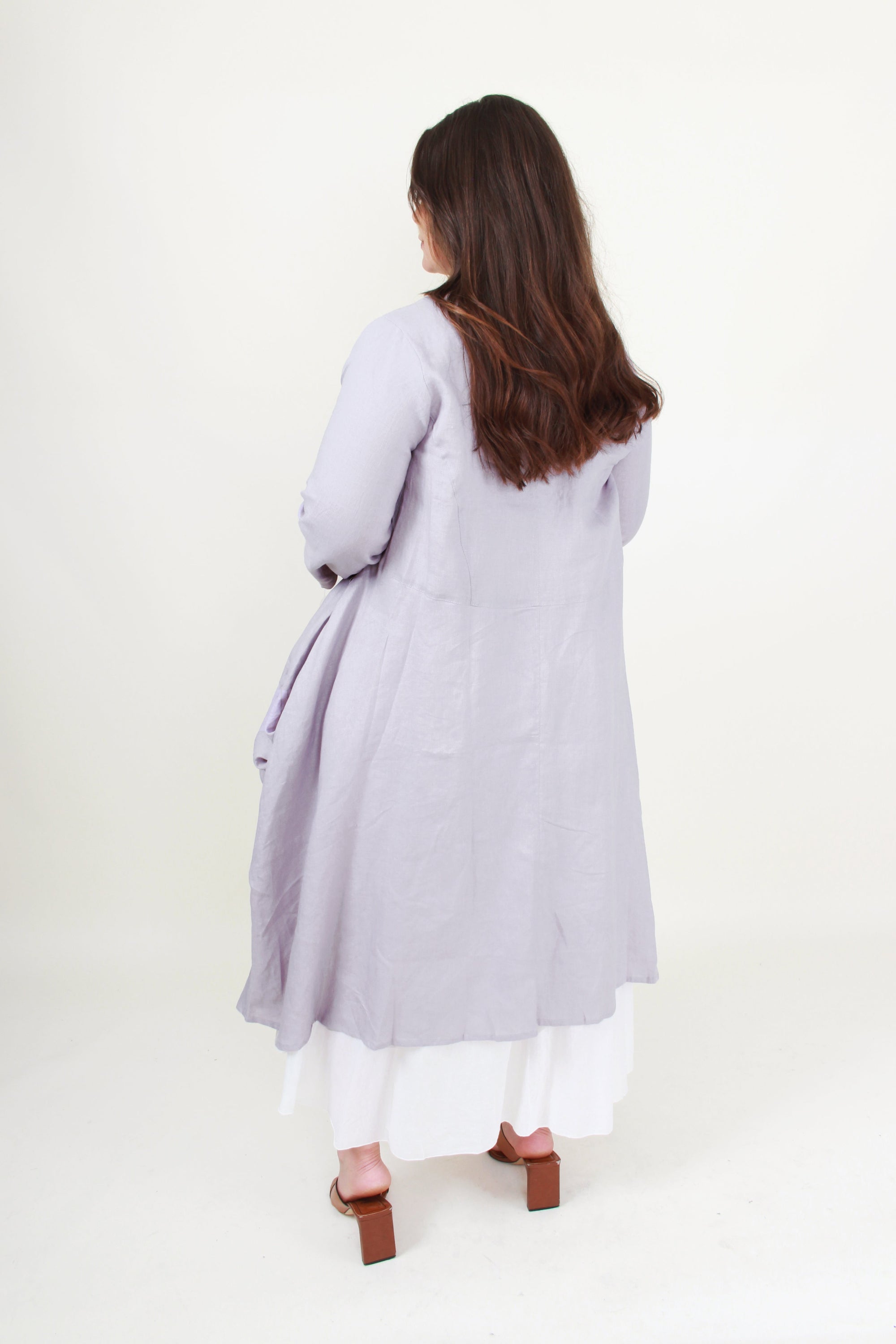 Woman wearing a light grey long coat on a white background back view