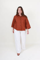 Woman wearing a rust-colored shirt and white pants on a white background