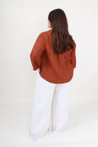 Person wearing a rust-colored shirt and white pants on a white background