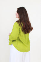 Woman wearing a green jacket and white pants against a white background back view