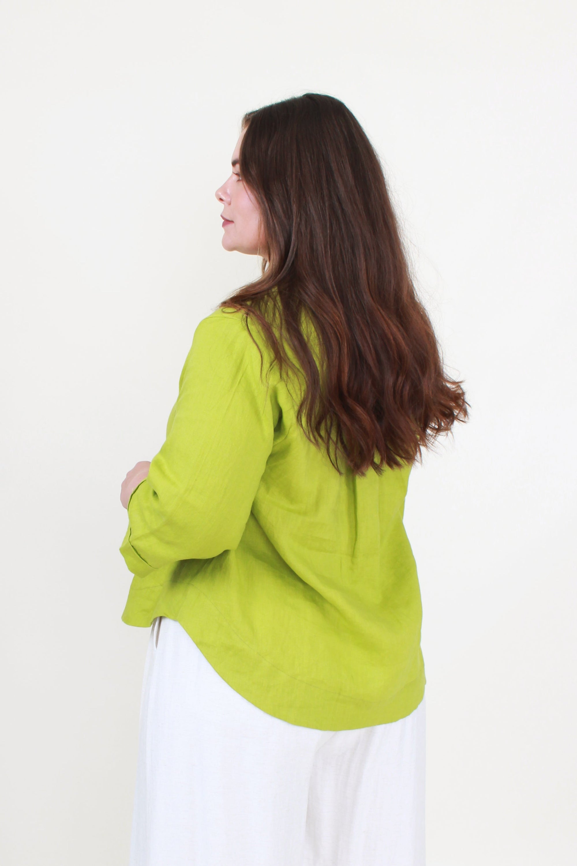 Woman wearing a green jacket and white pants against a white background back view