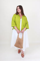 Woman wearing a green jacket and white dress holding a woven bag on a white background