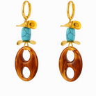 A pair of gold-tone drop earrings featuring a turquoise stone, a gold leaf-shaped charm, and a large oval amber resin dangle, set against a plain white background.