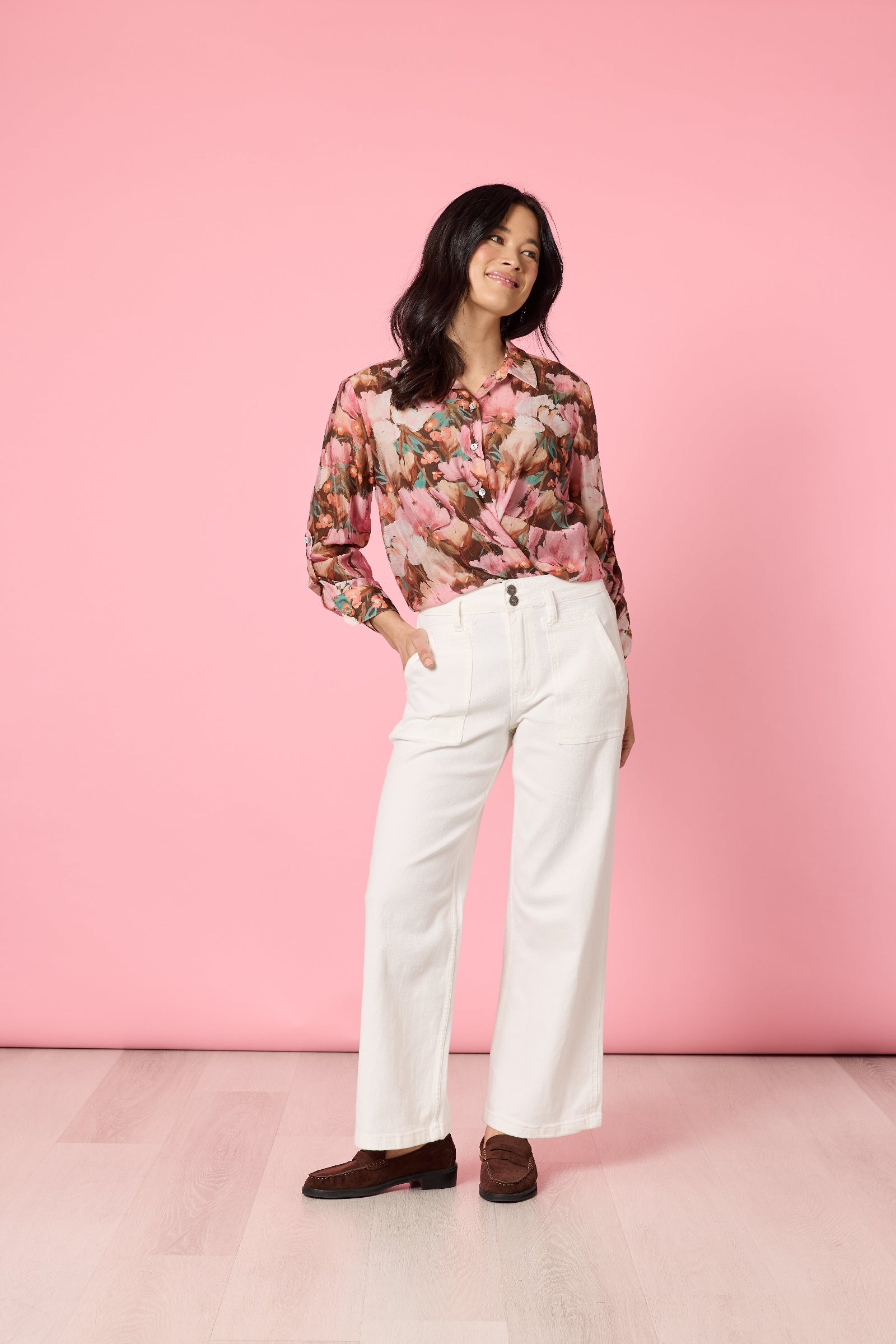 Woman wearing a floral blouse and white pants against a pink background