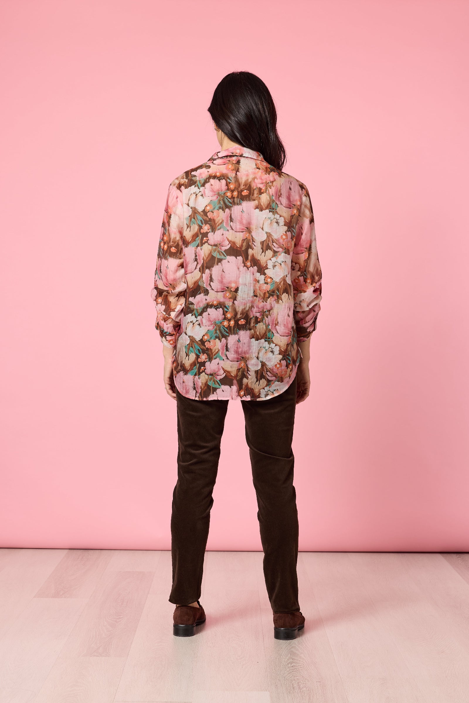 Person wearing a floral blouse and dark pants against a pink background