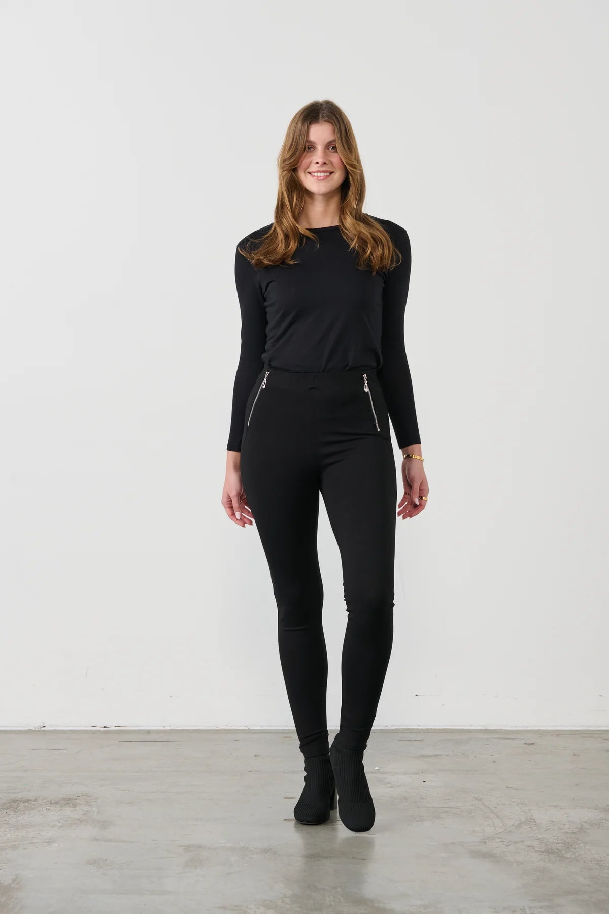 women wearing slim black pants and black top on a white background and gre floor