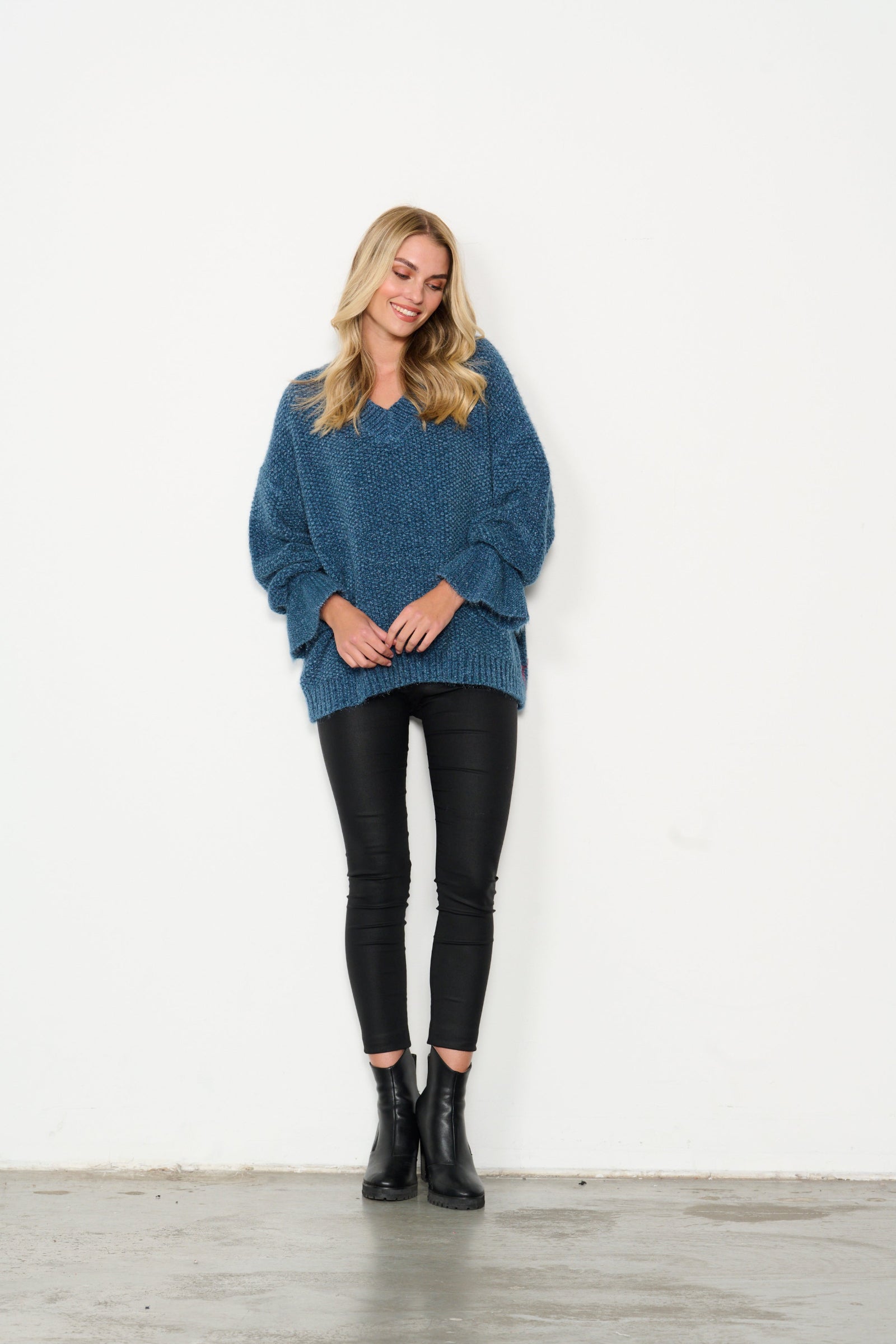 Woman wearing a blue sweater, black leggings, and black boots on a white background