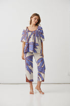A woman modeling a matching two-piece set featuring a short-sleeve top and cropped pants with a blue and brown tropical leaf print on a cream background, set against a plain white studio background.