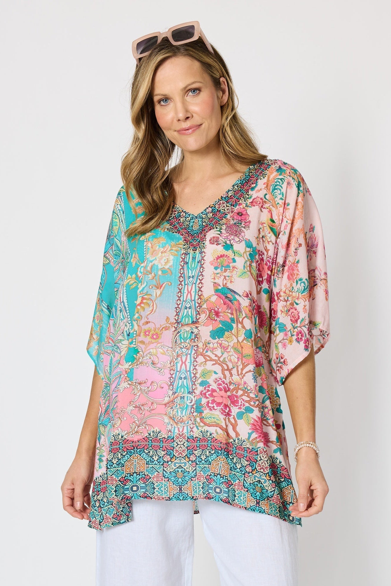 Woman wearing a colourful pink and blue printed floaty top with elbow length sleeves and detailed border and neckline.