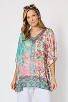 Woman wearing a colourful pink and blue printed floaty top with elbow length sleeves and detailed border and neckline.