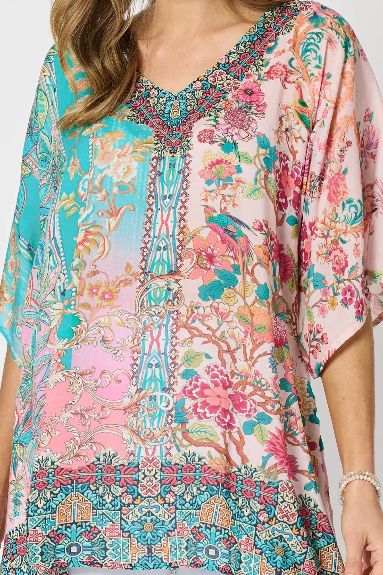 Woman wearing a colourful pink and blue printed floaty top with elbow length sleeves and detailed border and neckline.